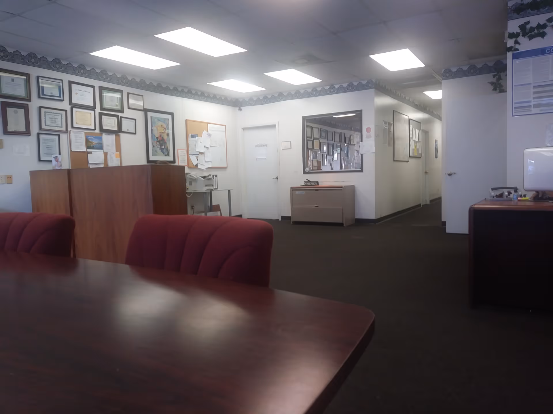 Interior lobby area with burgundy chairs, a table, and framed certificates.