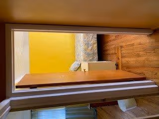 View through a doorway into a small bedroom with a bed covered in a floral blanket, a nightstand, and hardwood floor.