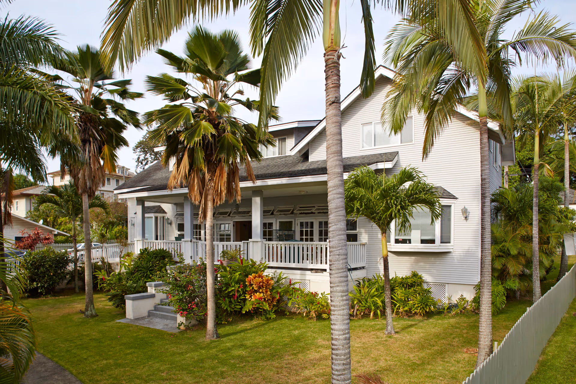 White, two-story senior care home with a porch, palm trees, and tropical landscaping.