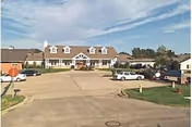 Front view of Sunshine Meadows Retirement Community building with a driveway and parked cars.