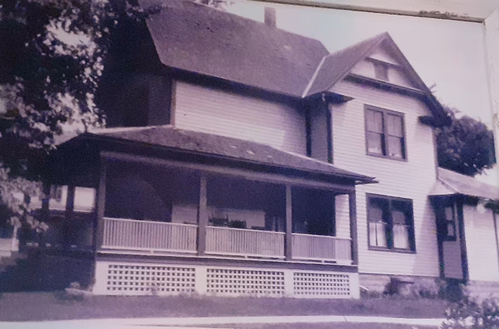 Vintage two-story house with a wraparound porch, lattice foundation, and light siding exterior.