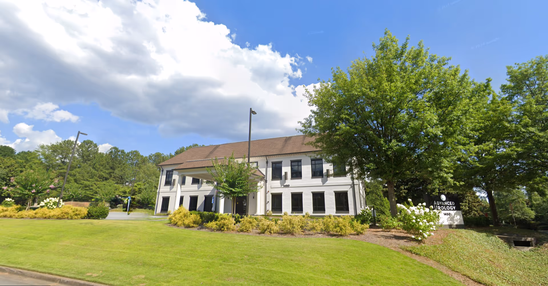 A white two-story building with a brown roof sits on a manicured lawn surrounded by trees.