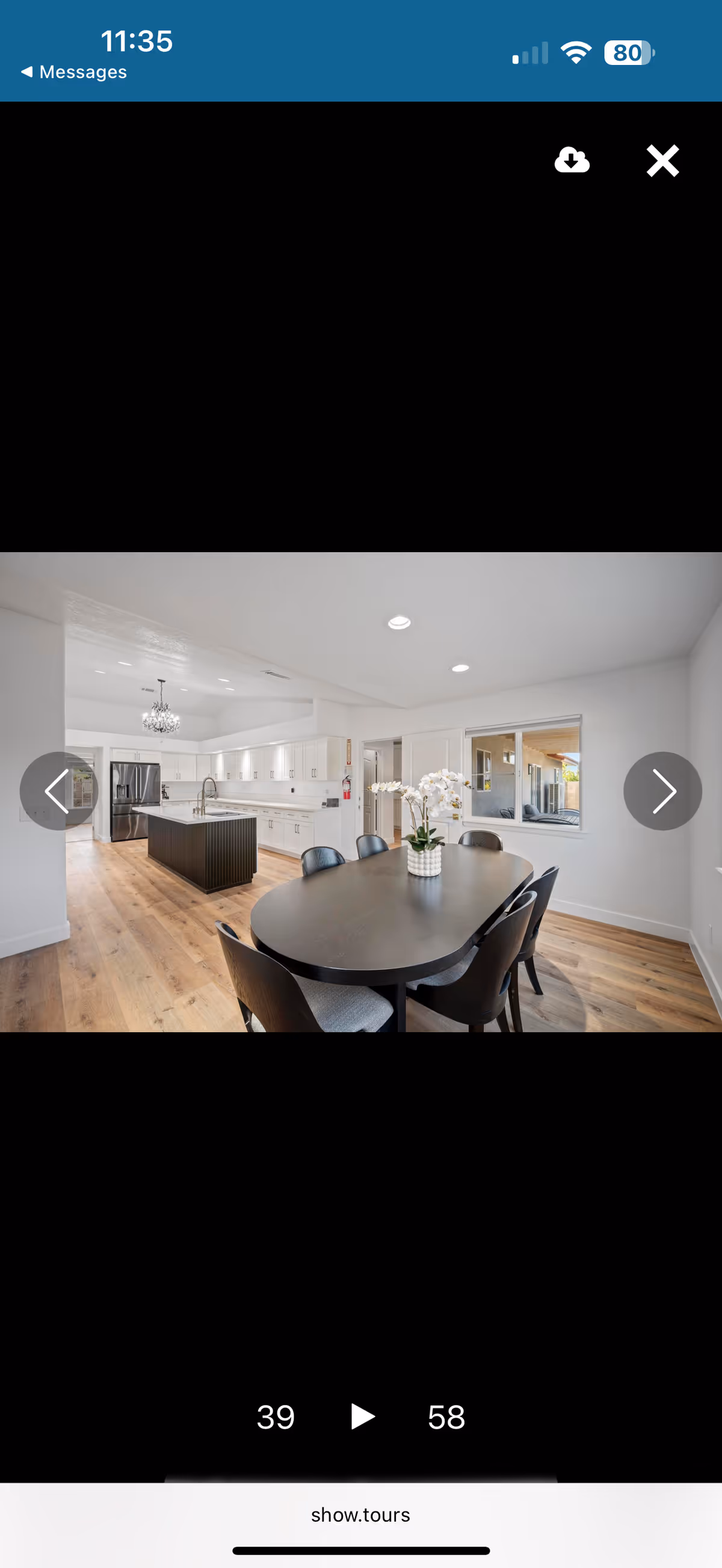 Modern dining room with dark oval table, chairs, orchid centerpiece, and white kitchen in background.