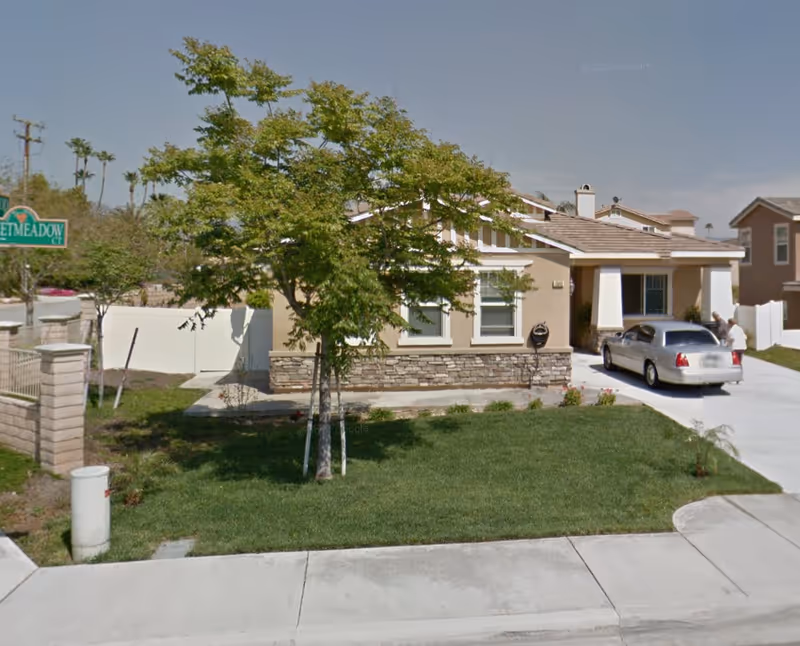 Suburban single-story beige house with stone accent, driveway, and a parked silver car.