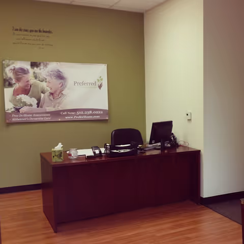 Reception area with a dark wood desk, computer, and wall poster for Preferred Care.