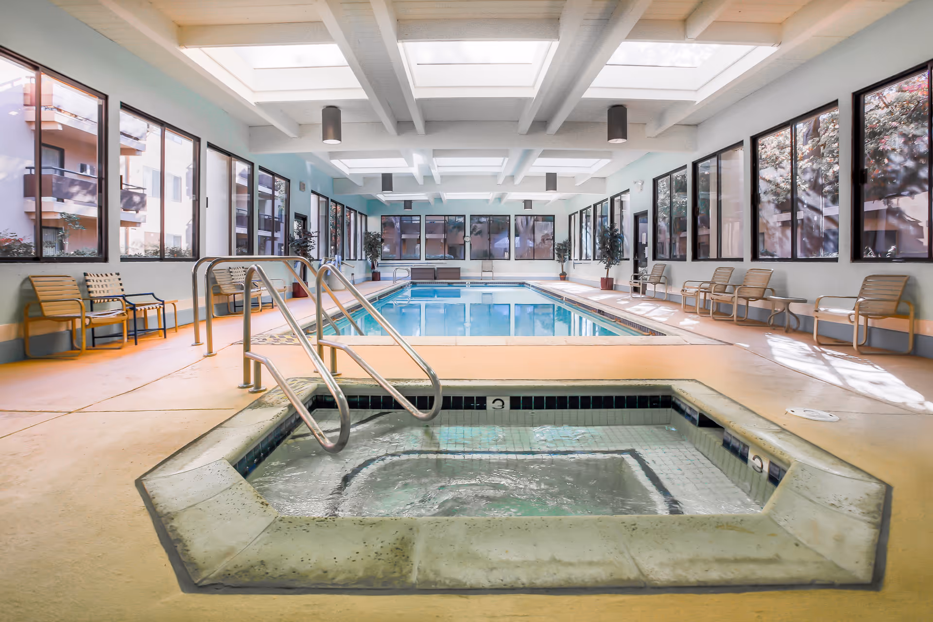 Indoor pool area with a hot tub and skylights, lined with lounge chairs.