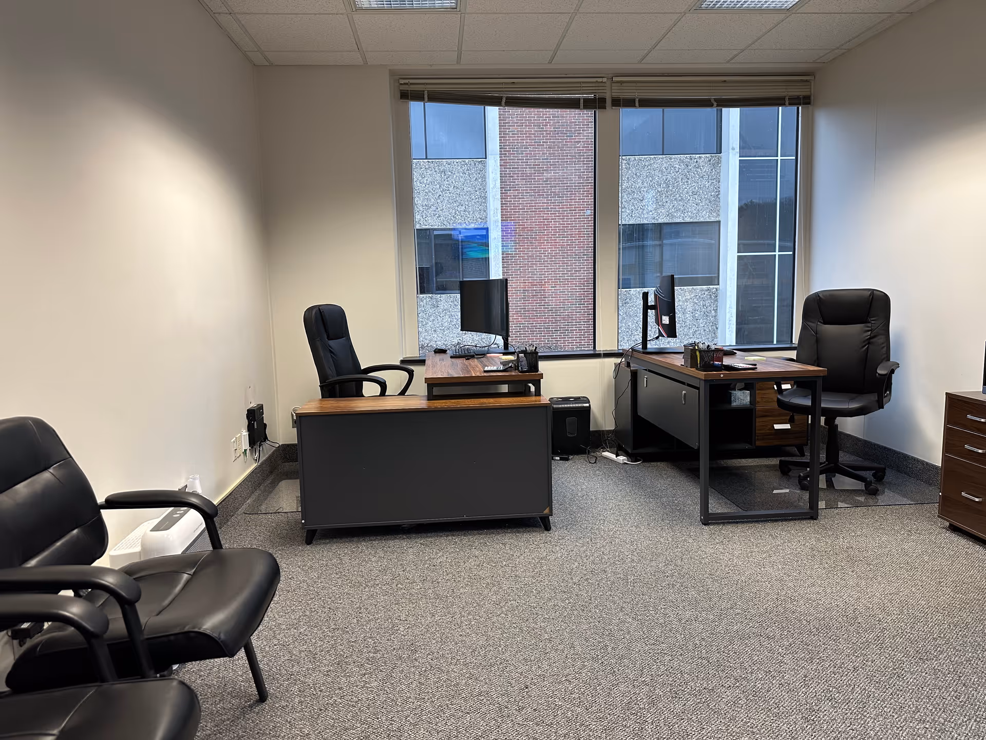 Empty office space with two desks, chairs, computers, and a large window view.