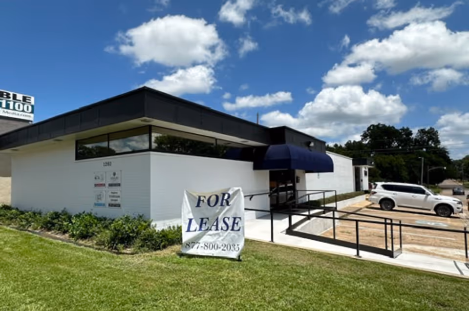 White brick senior facility exterior with blue awning and a large 'For Lease' sign