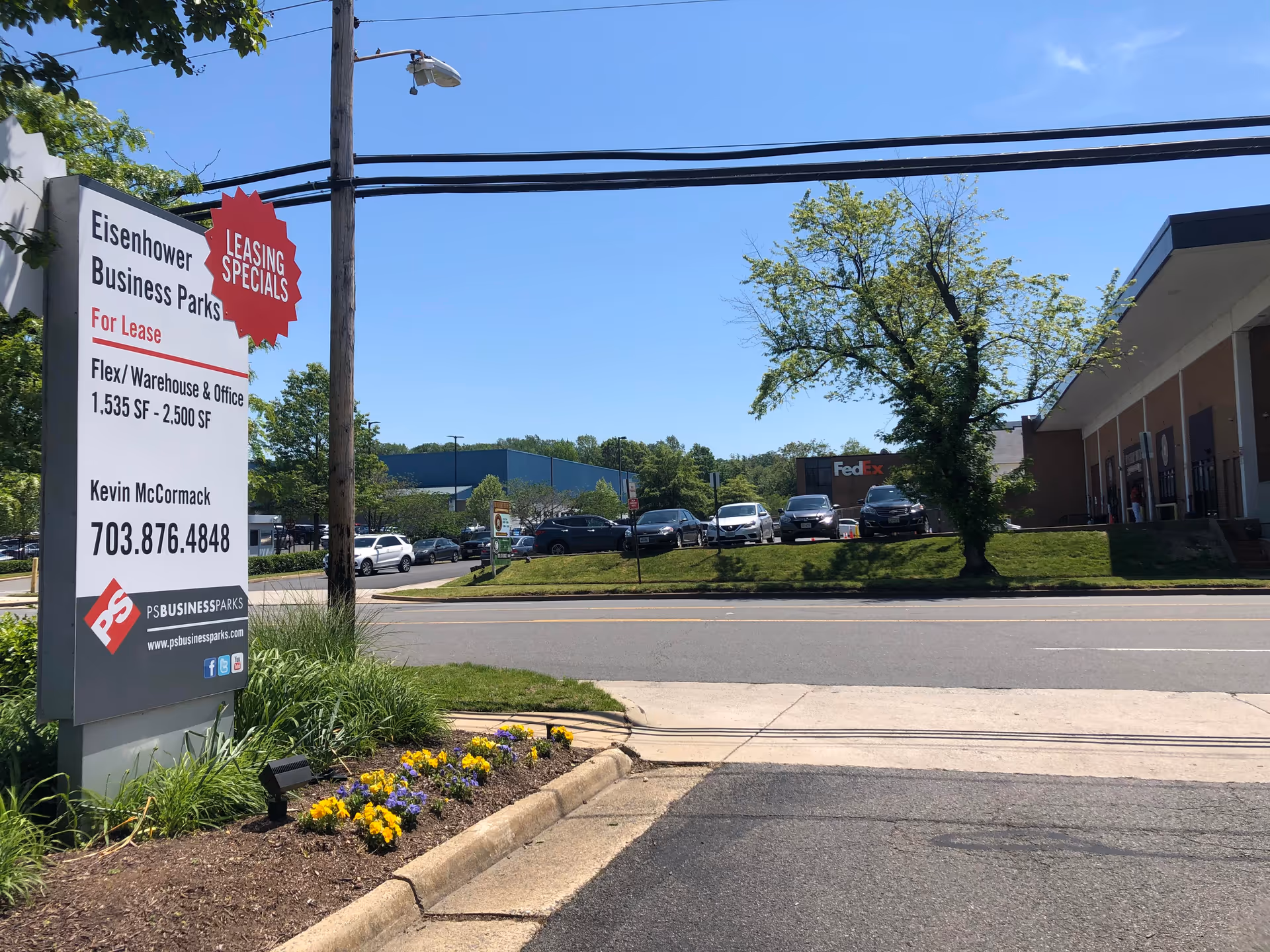 Wide exterior street view with a leasing sign, adjacent building, and parked cars.