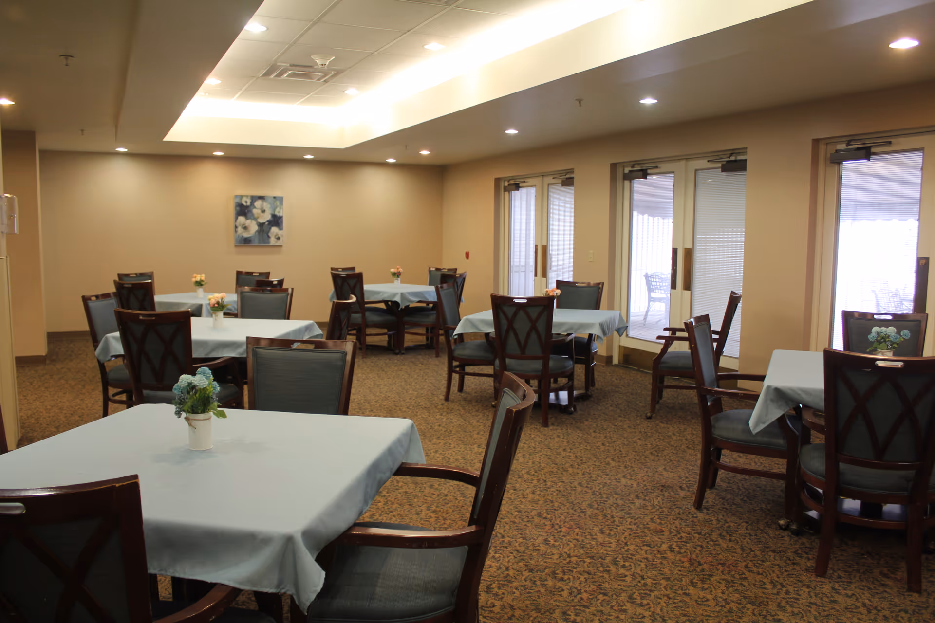 Bright dining room with multiple tables covered in light blue tablecloths and chairs.