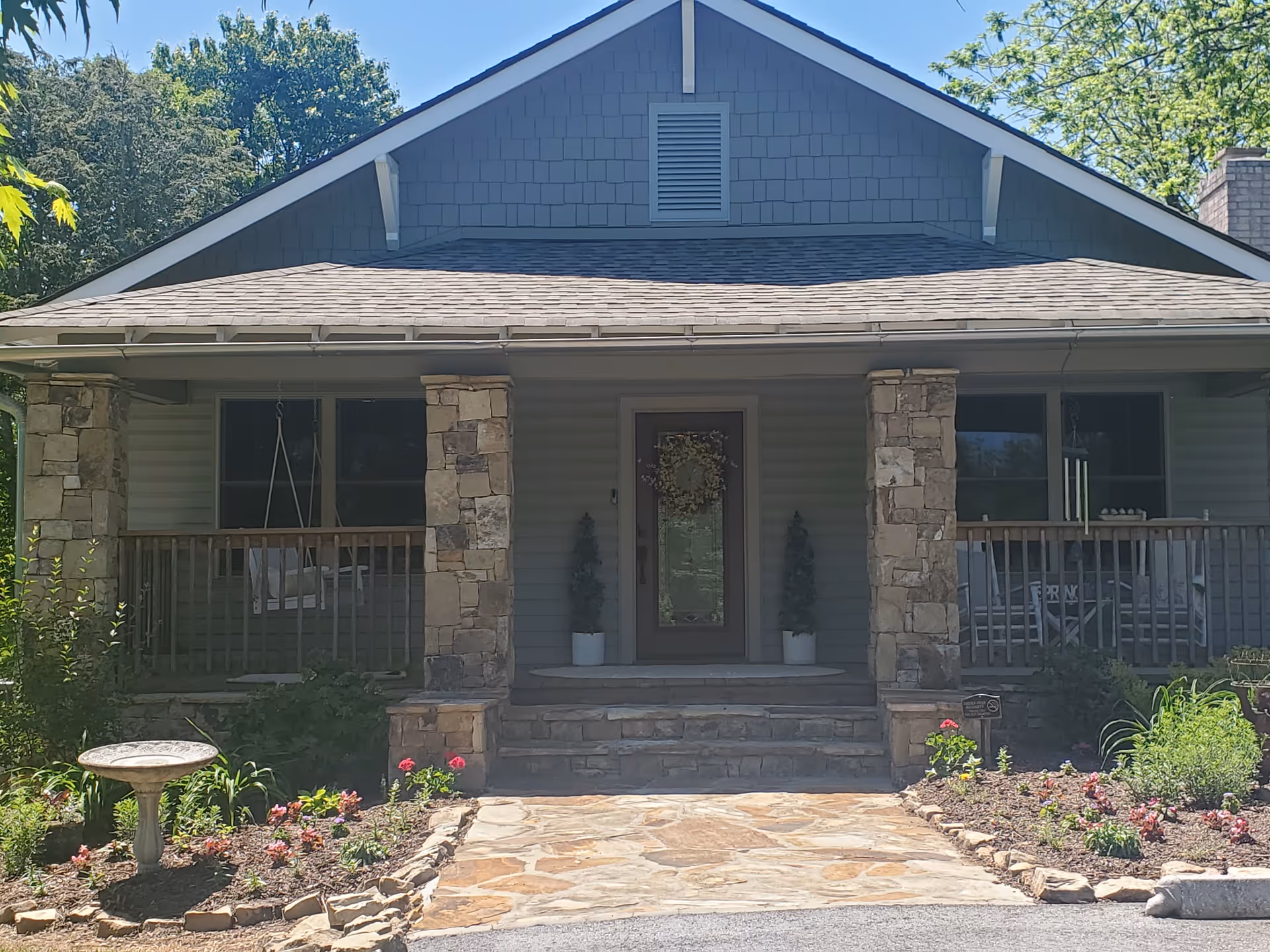 Front view of a stone-porch facility with garden and porch swing.