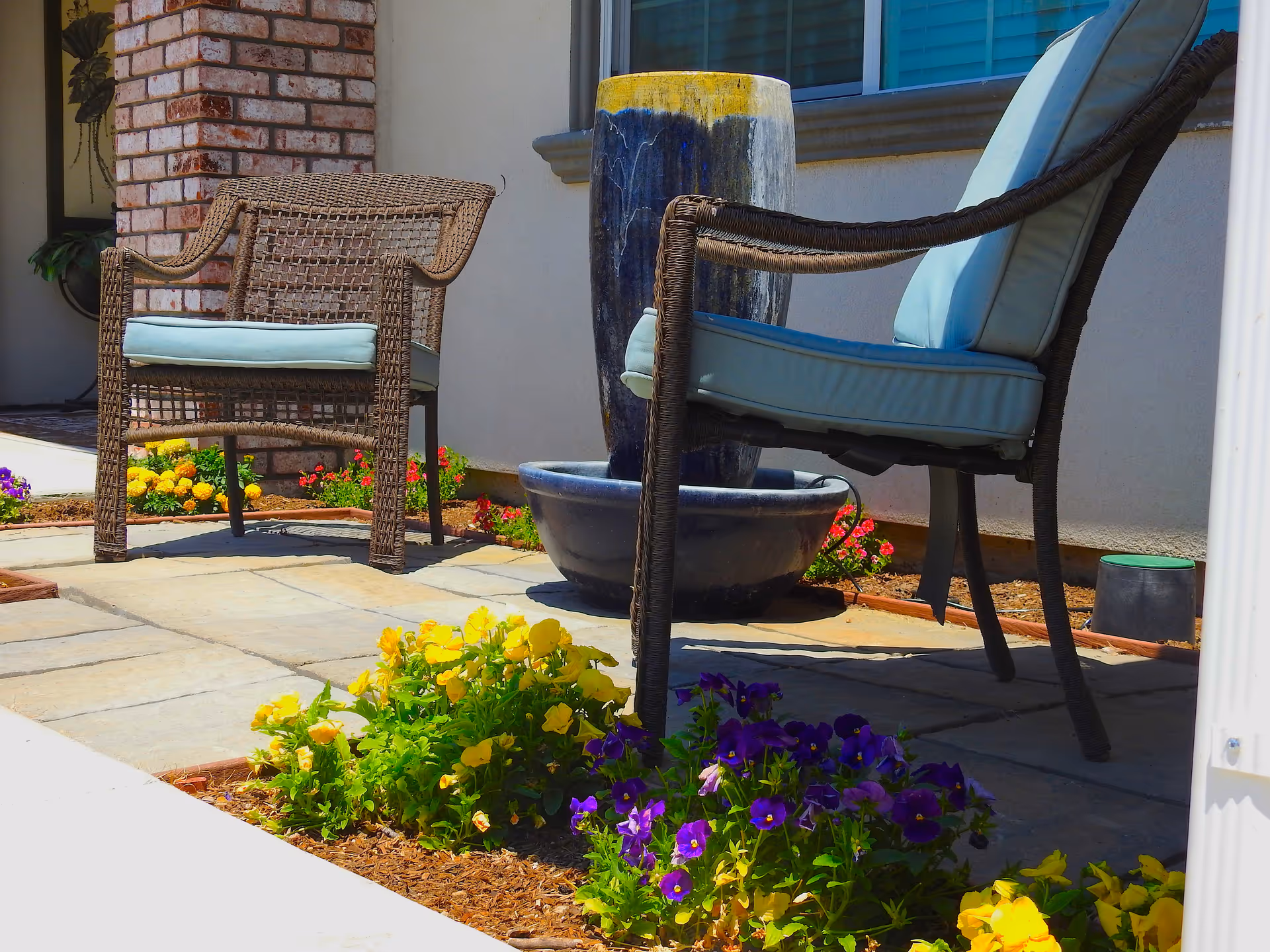 Outdoor patio with wicker chairs, a large planter, and colorful flowers in bloom.