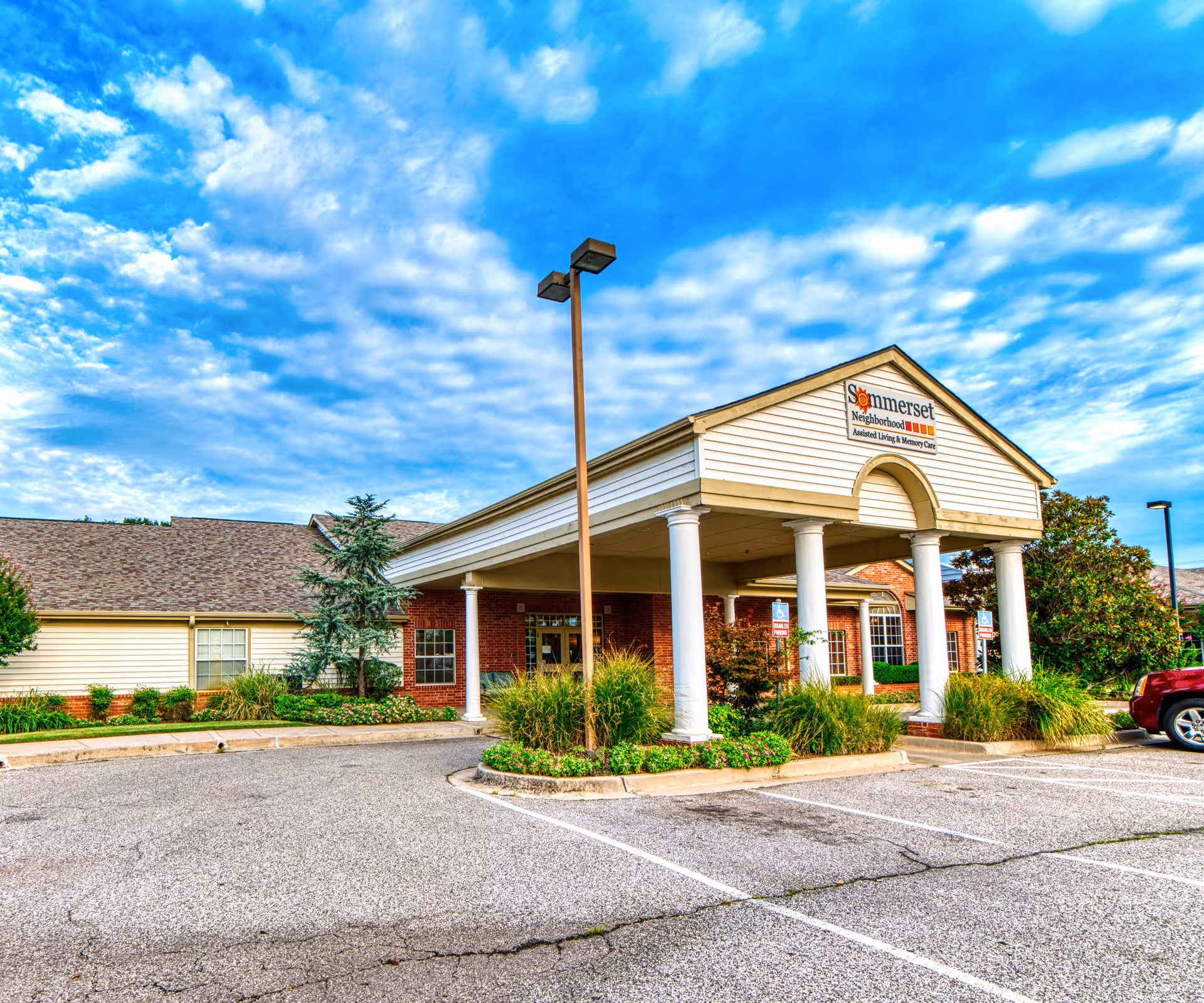 Sunny exterior of Somerset Neighborhood senior living facility with a covered entrance and parking.