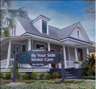 Gray two-story house with a sign reading By Your Side Senior Care in front yard.