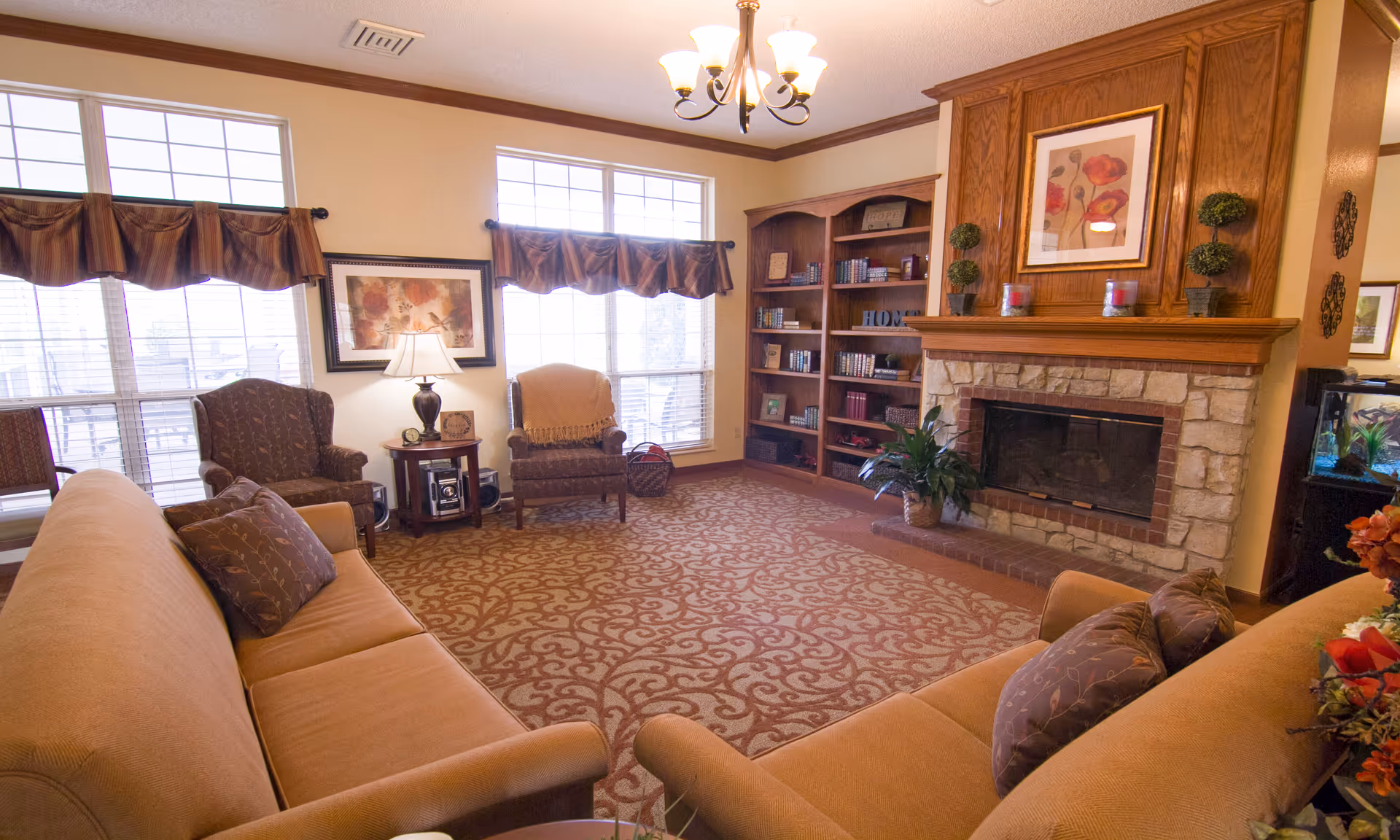 Cozy resident lounge with sofas, a fireplace, bookshelves, and warm decor.