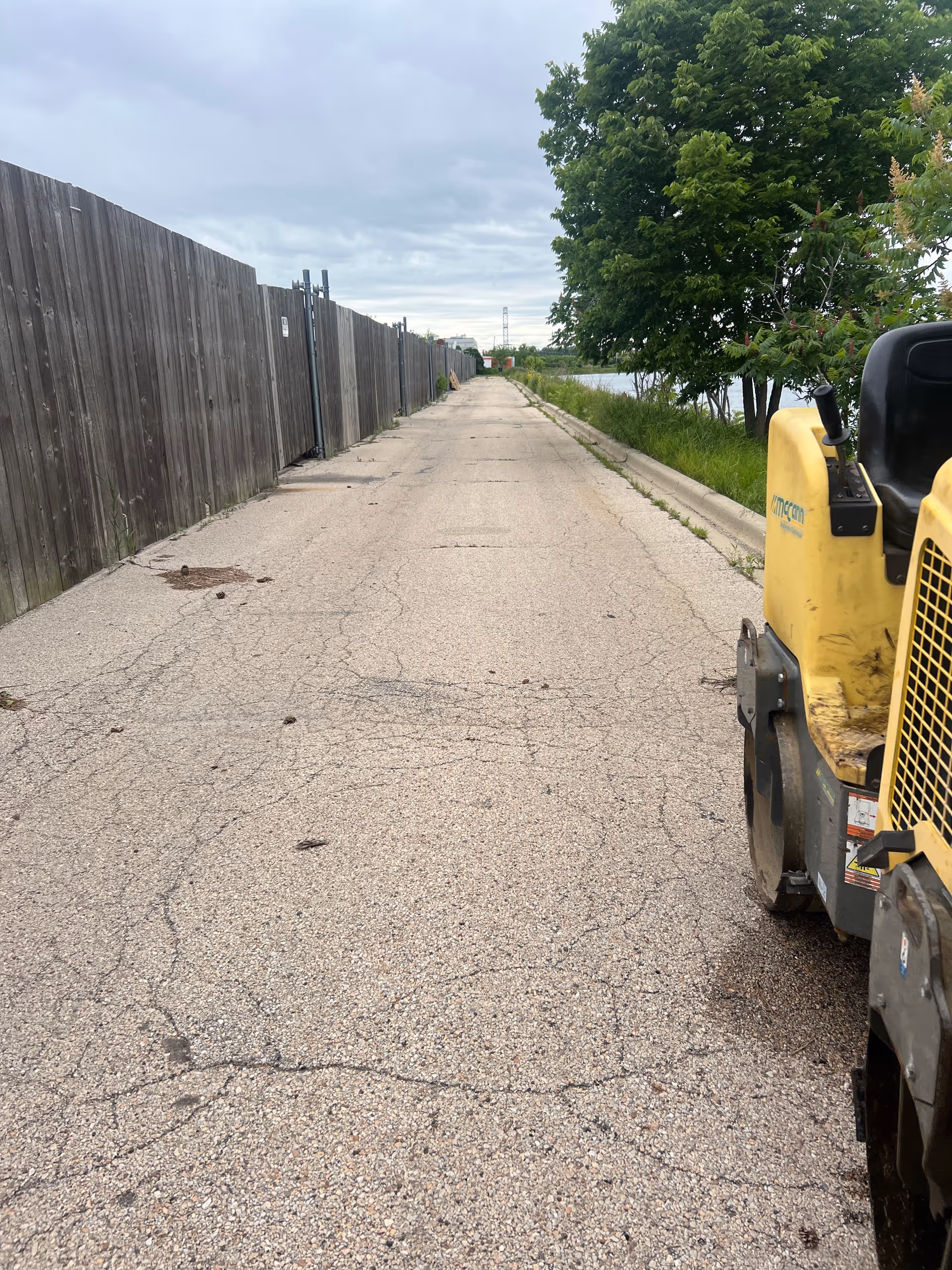 Long outdoor alley with a wooden fence, trees, and a yellow construction machine.