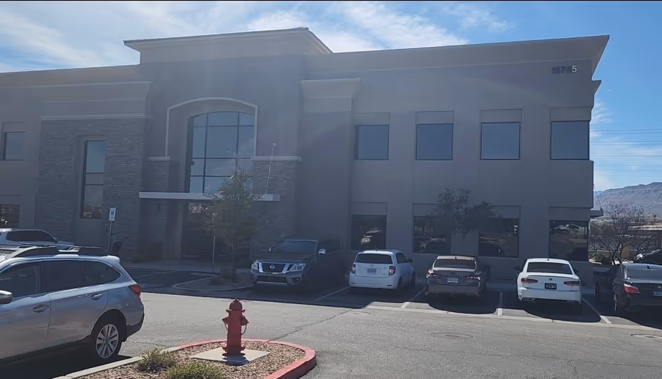 Modern stone and plaster building exterior with parked cars in front and blue sky.