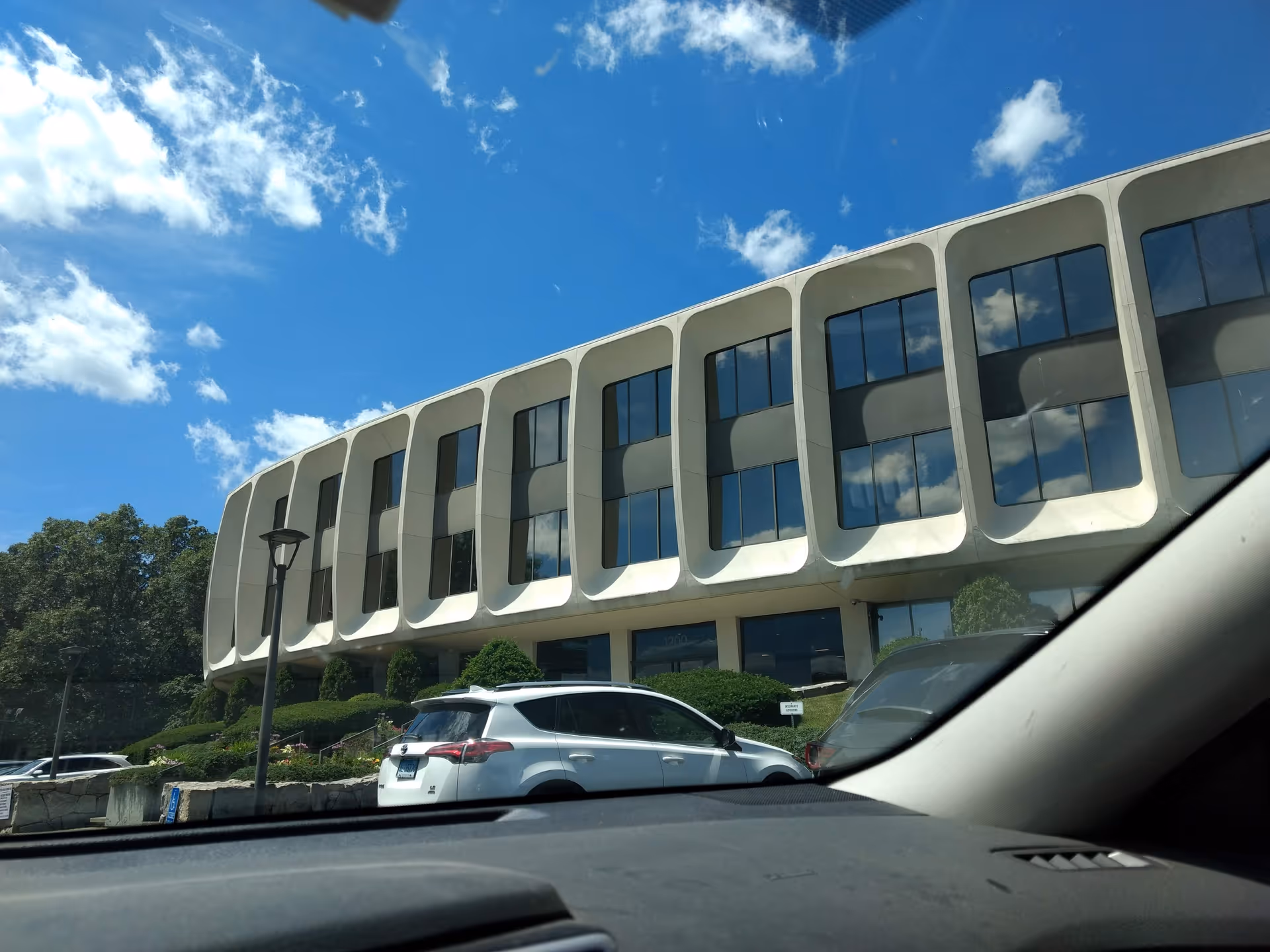 Exterior view of a modern white building with curved window frames and a parking lot.
