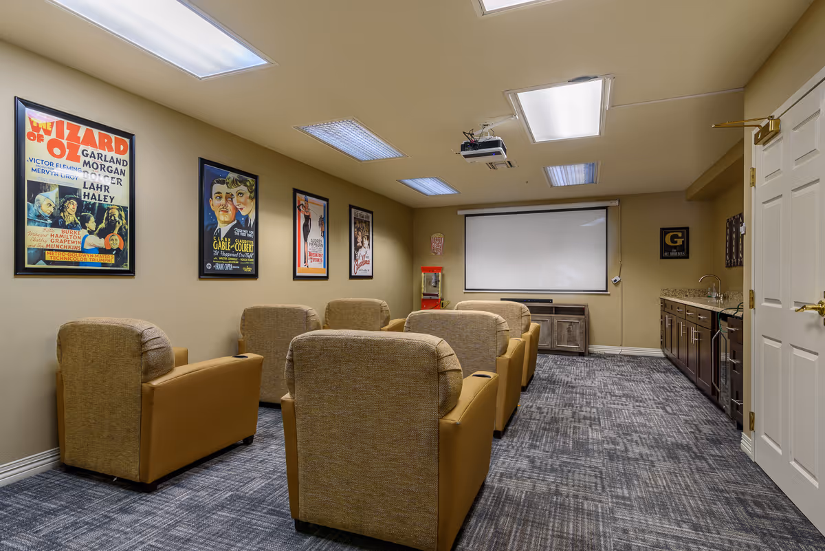 A lounge room with several beige armchairs, movie posters, a projector, and a kitchenette.