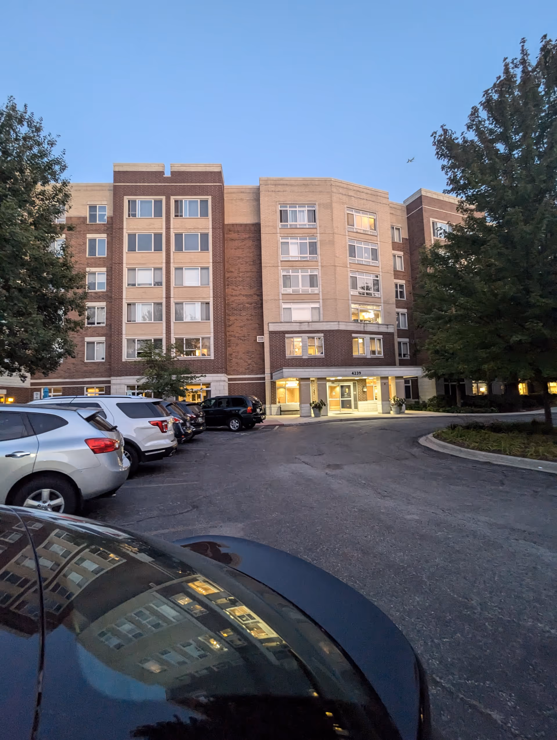 Front view of a multi-story brick senior living building with cars parked outside.