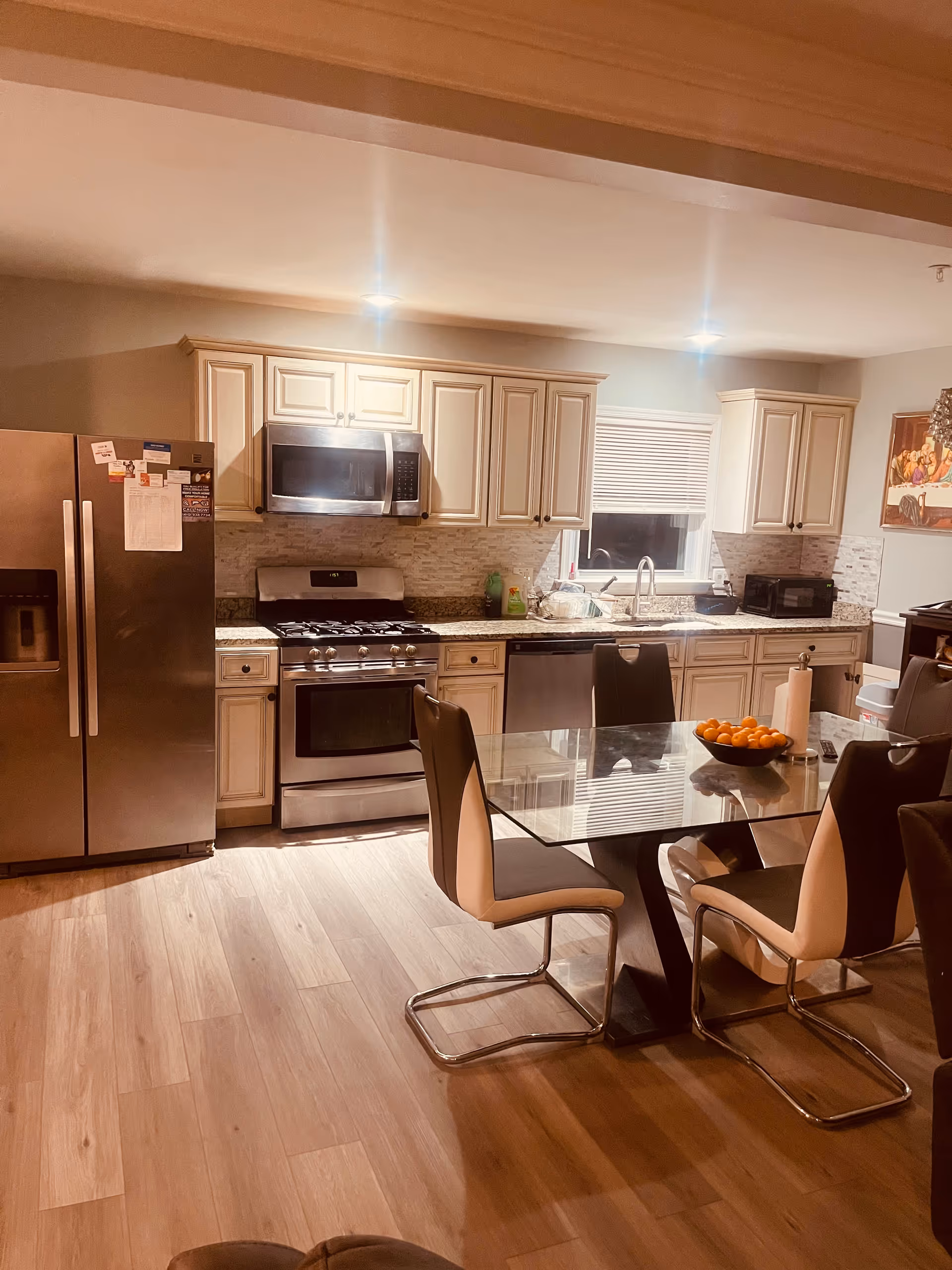 A modern kitchen with stainless steel appliances, glass dining table, and beige chairs.