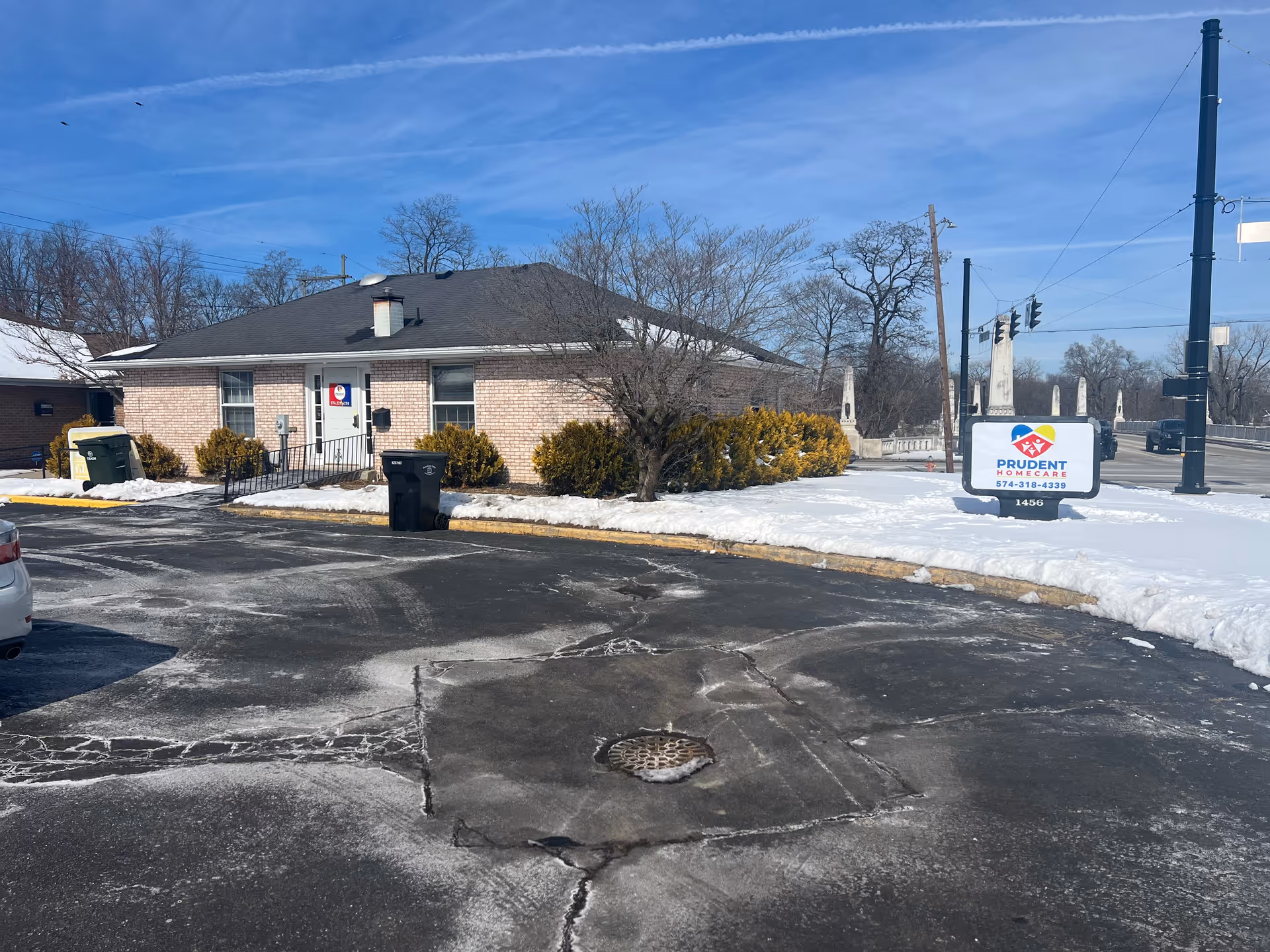 Exterior view of a single-story brick facility with a Prudent Home Care sign and snow.