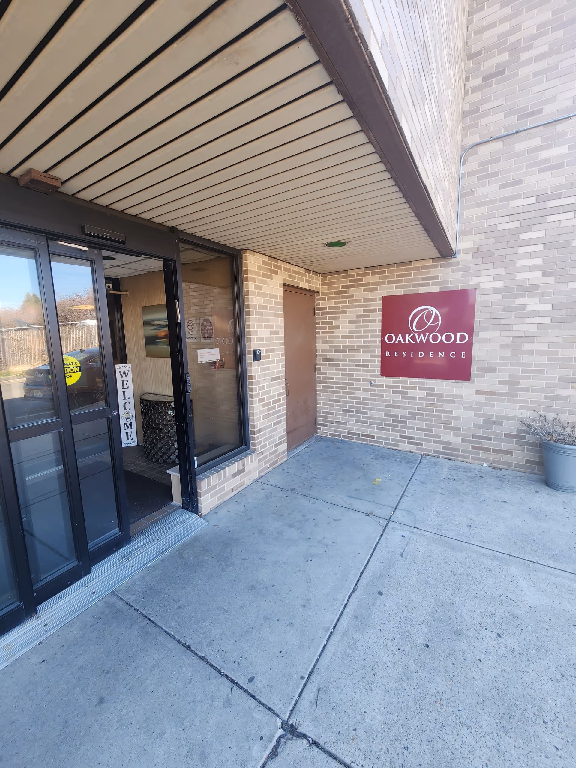 Brick exterior of Oakwood Residence entrance with glass doors and a maroon Oakwood sign.