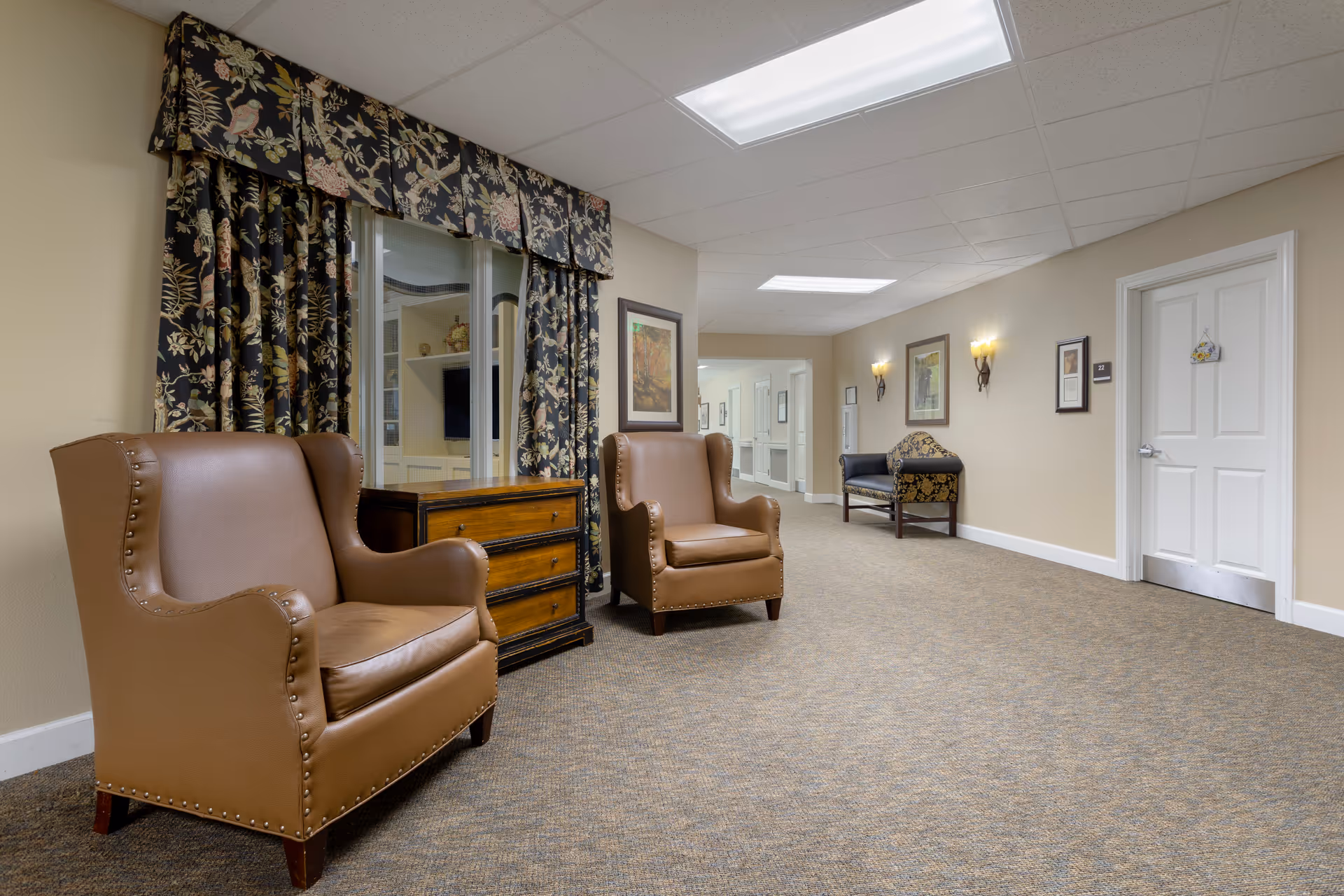 Interior lounge area with two brown leather chairs, a dresser, and floral curtains.