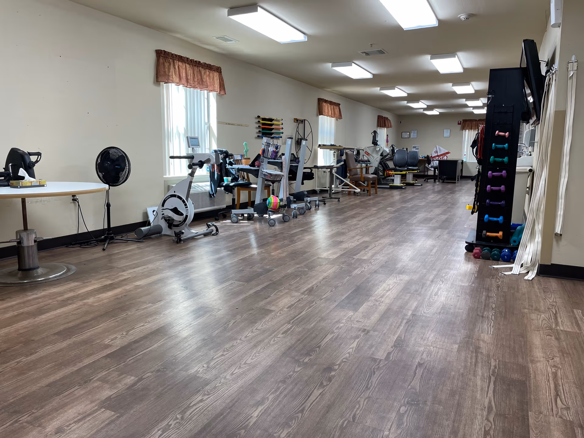 Long rehabilitation gym with exercise equipment, bikes, and weights along the wall.