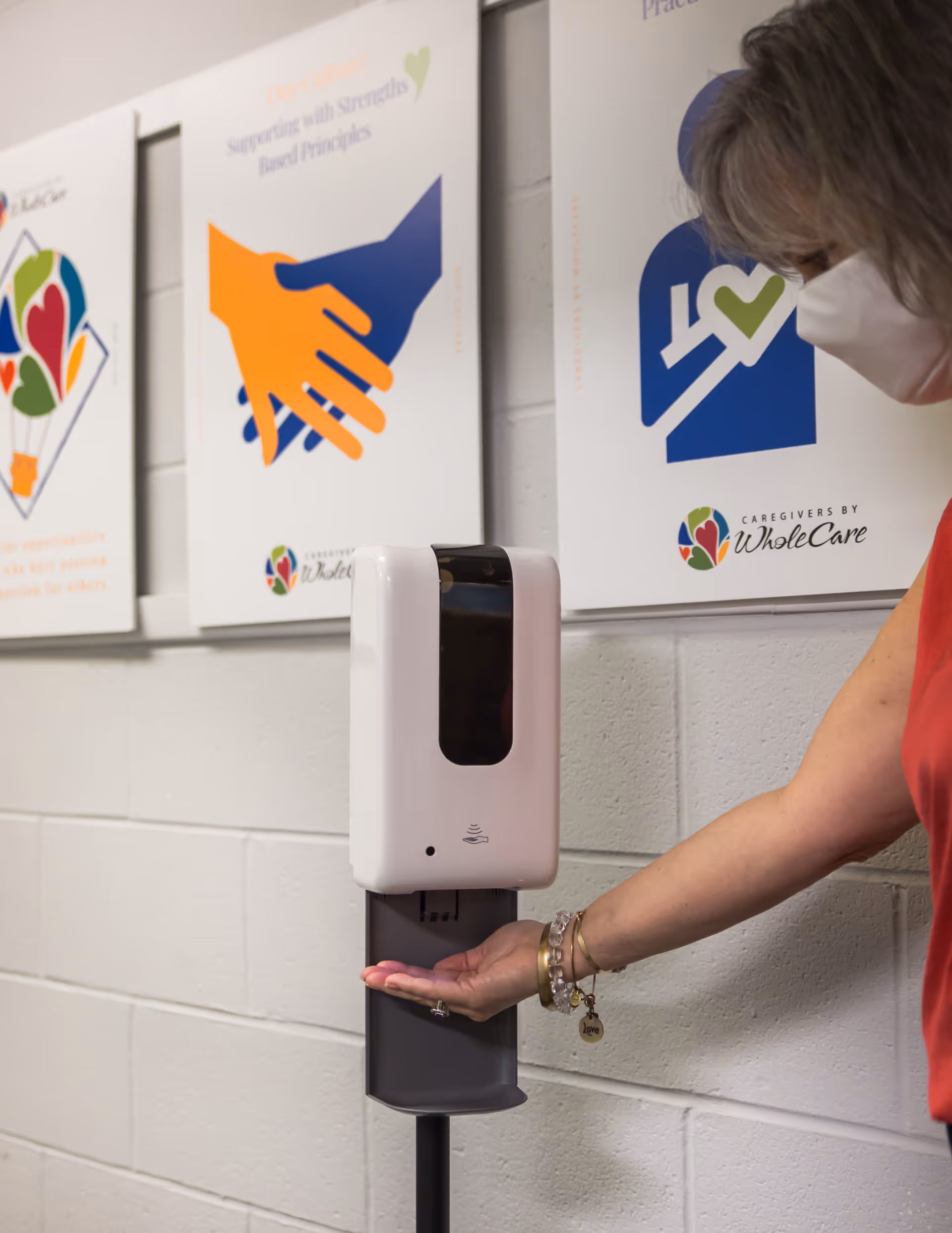 Wall-mounted hand sanitizer dispenser beside posters in an indoor senior living facility.