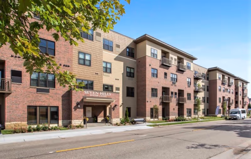 Front exterior of the multi-story Seven Hills Senior Living building with brick and tan siding along a street.
