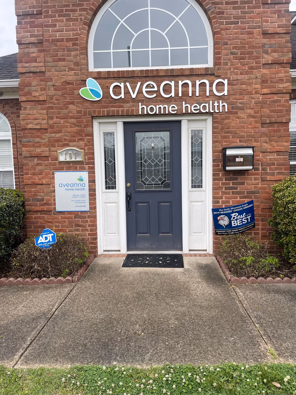 Brick building entrance with Aveanna Home Health sign and glass door.