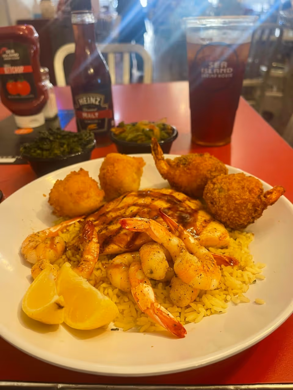 Plate of shrimp, rice, and fried items on a red table with drinks in the background.