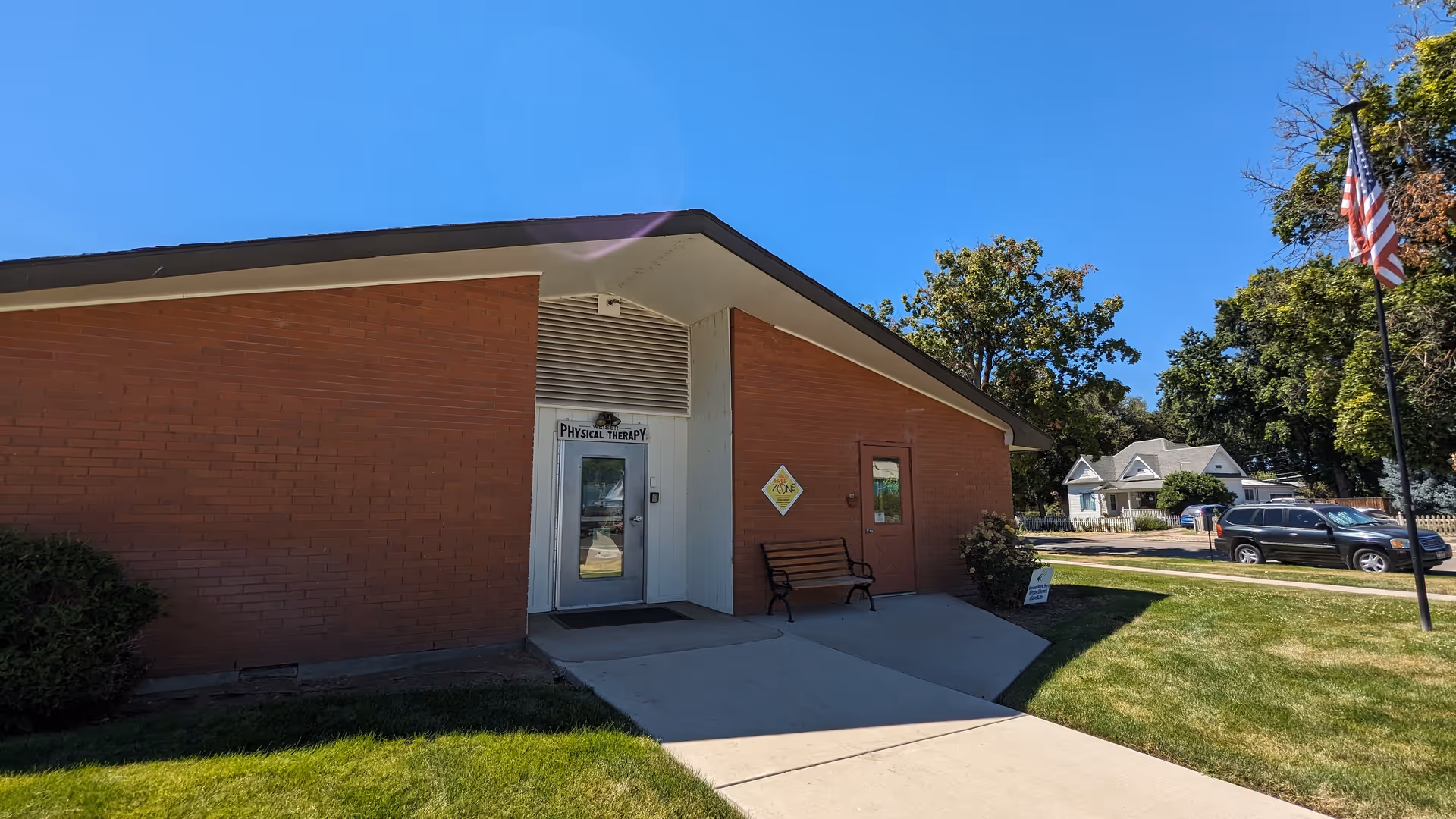 Brick building exterior with a door labeled Physical Therapy and a bench outside.
