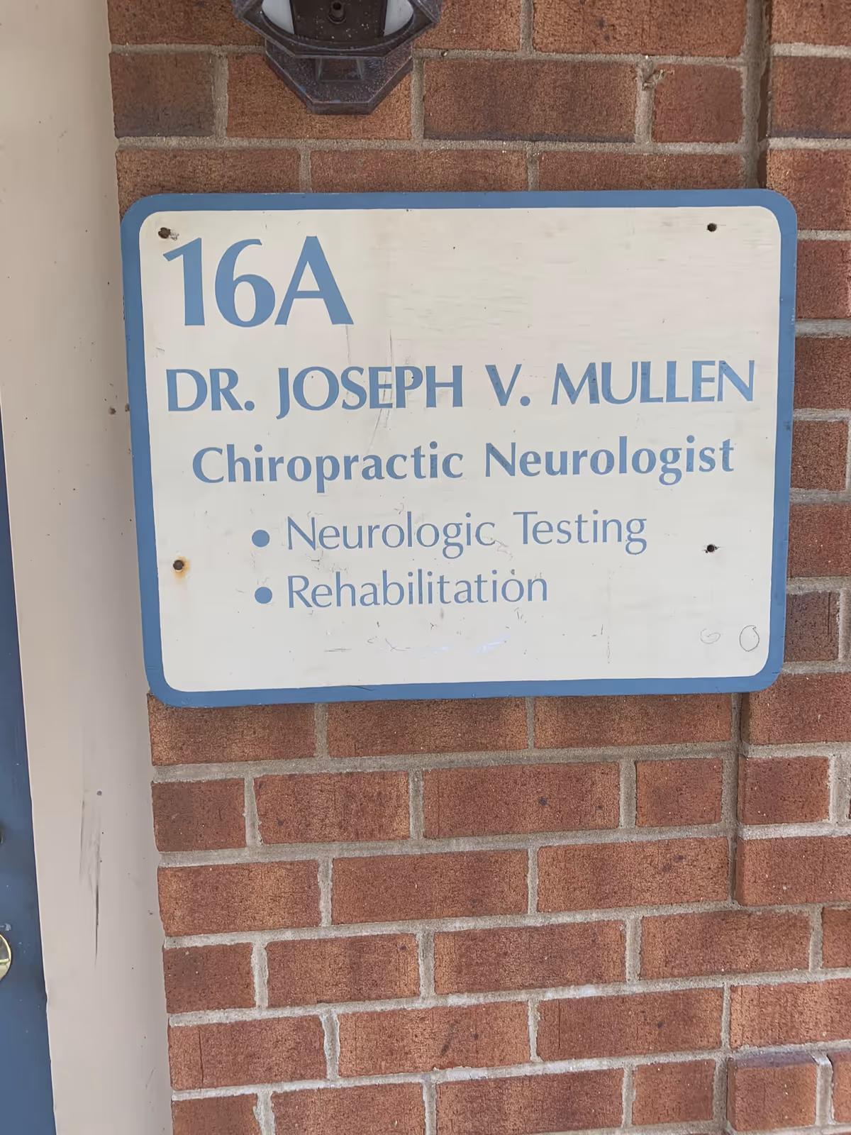 Exterior brick wall with a blue-framed sign for Dr. Joseph V. Mullen Chiropractor