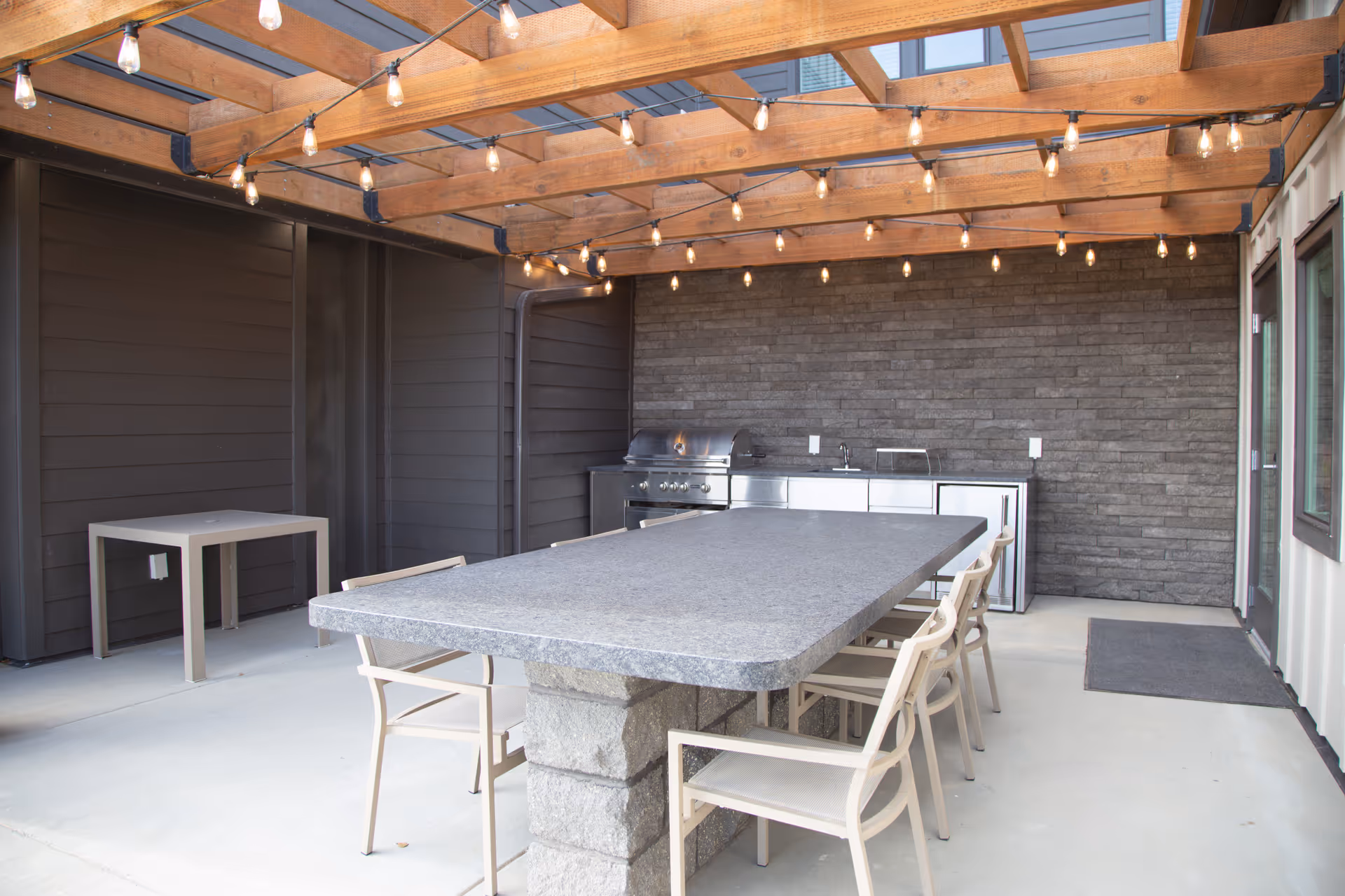 Outdoor patio with a long granite table, string lights, and built-in grill area.