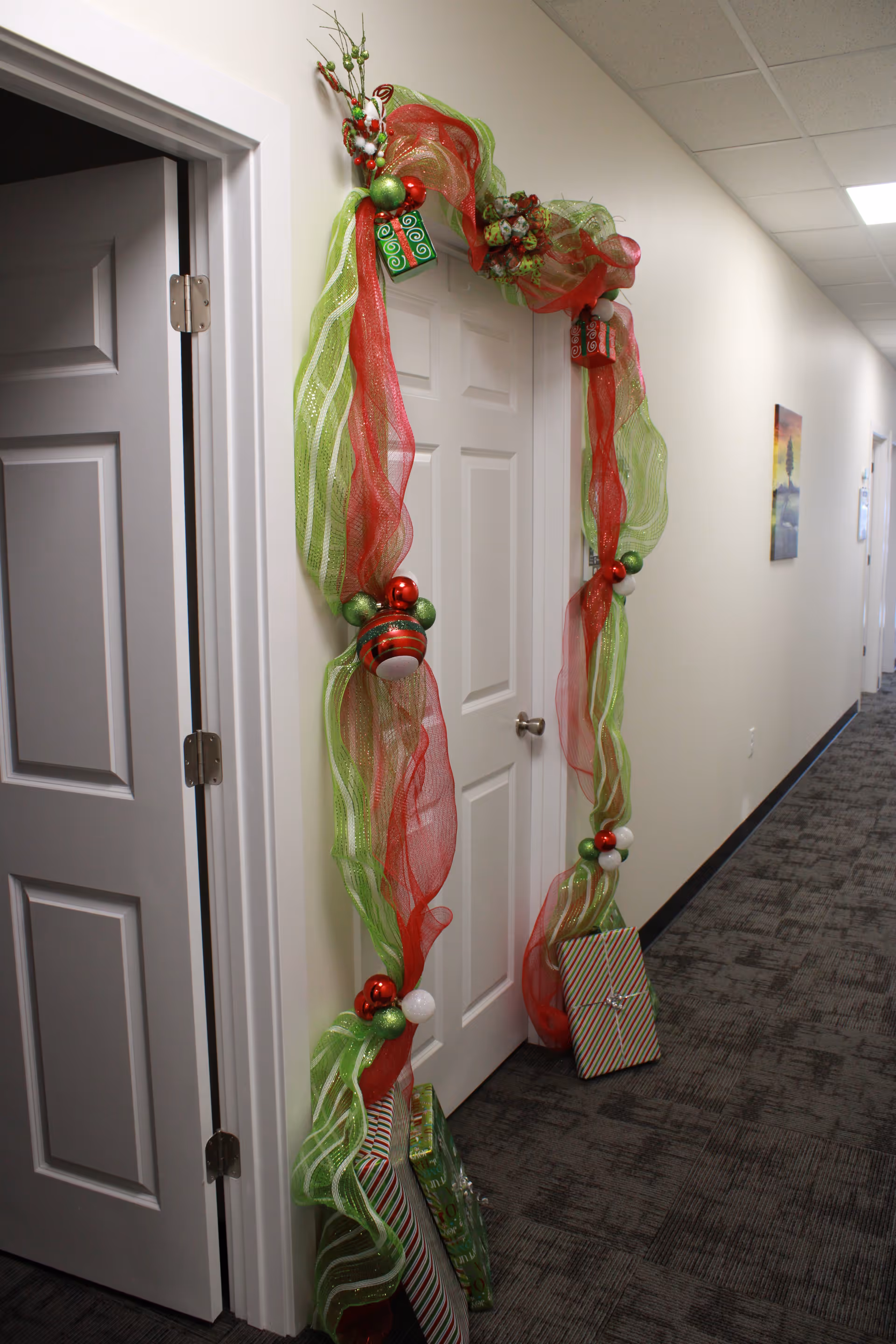 Festive red and green garland frames a door in a quiet hallway with gifts.