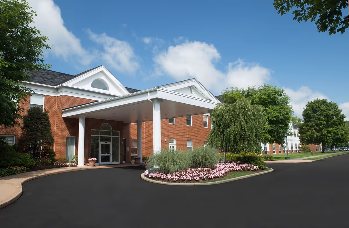 Wingate at Sudbury senior living facility exterior with columns, entrance canopy, and landscaped beds.