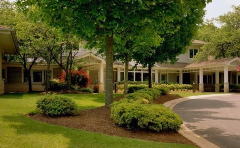 Front entrance and landscaped driveway of Raphael House with trees, shrubs, and a covered walkway.