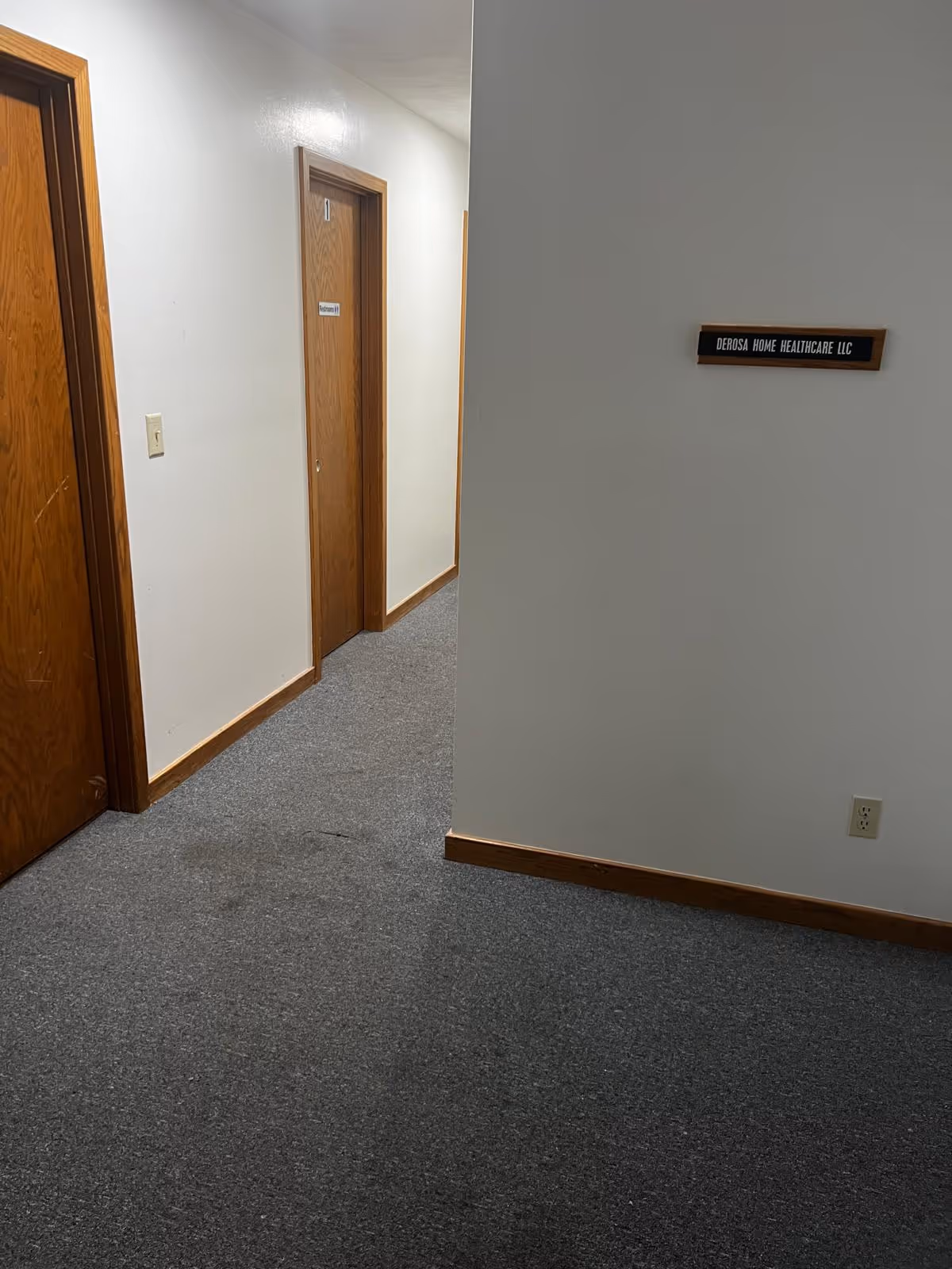 Interior hallway of a senior facility with wooden doors and a wall sign.