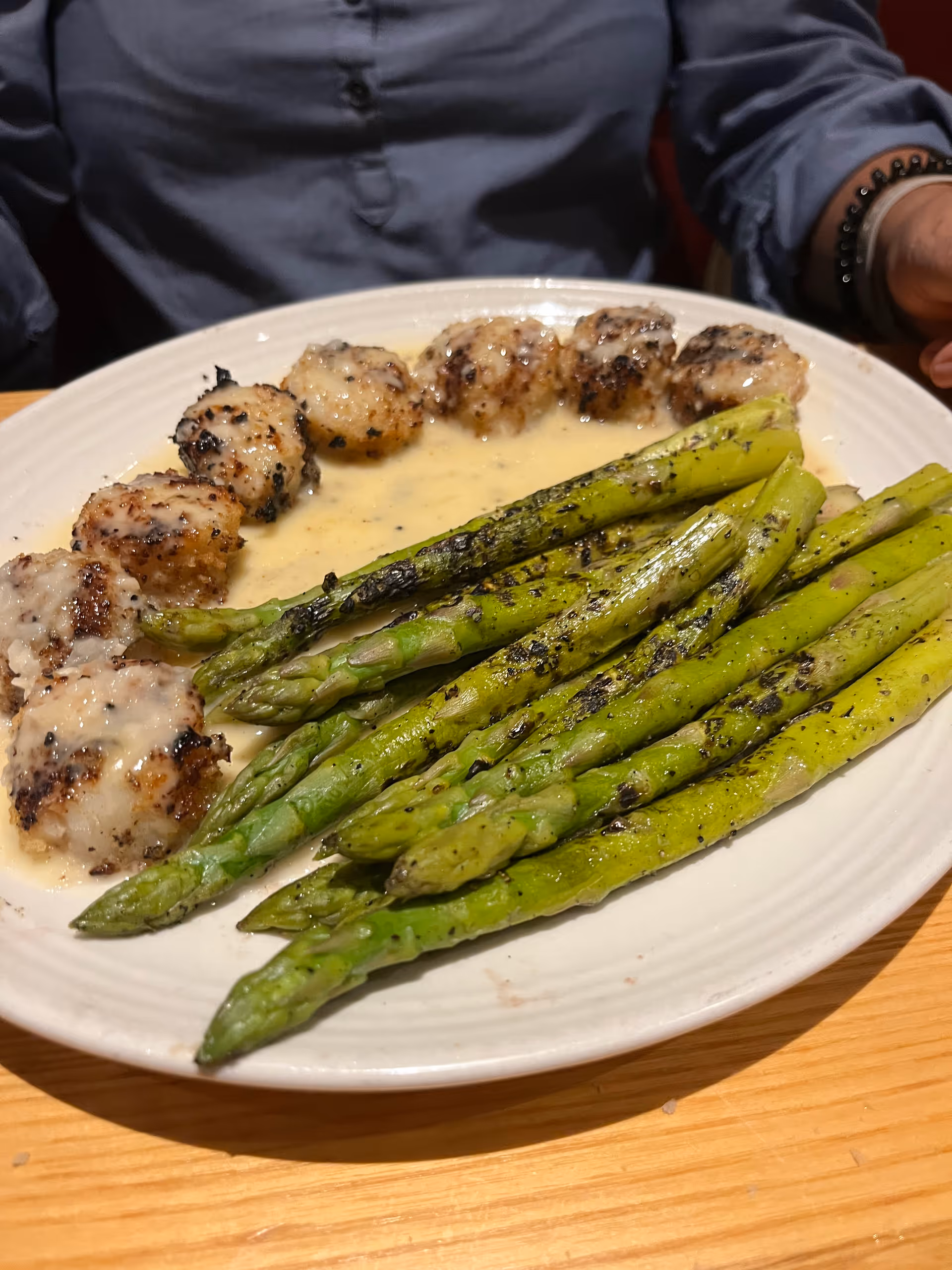 Plate of grilled asparagus and meatballs with sauce, with a person in the background.