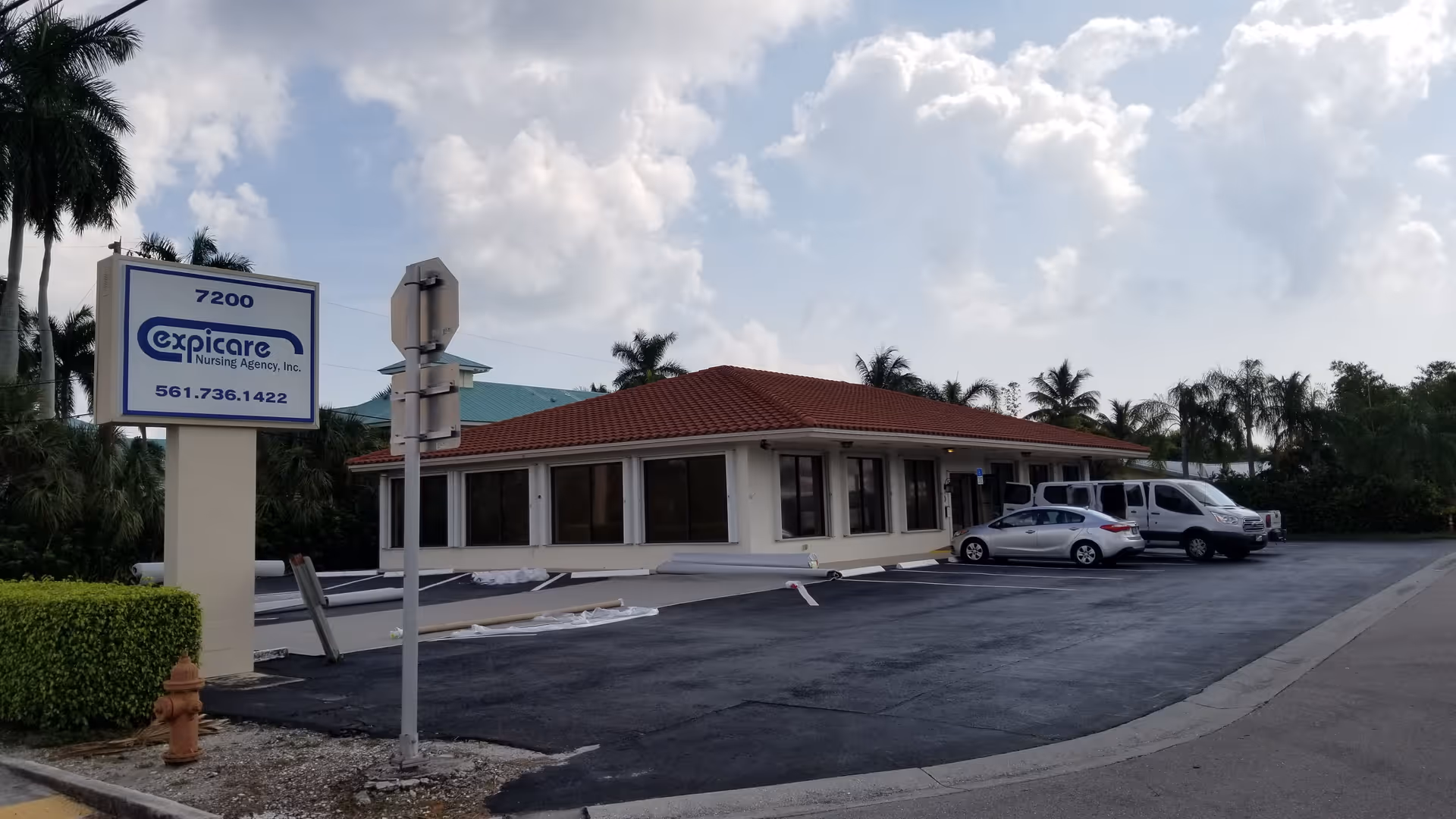 Exterior view of a single-story Expicare nursing facility with a parking lot and palm trees.