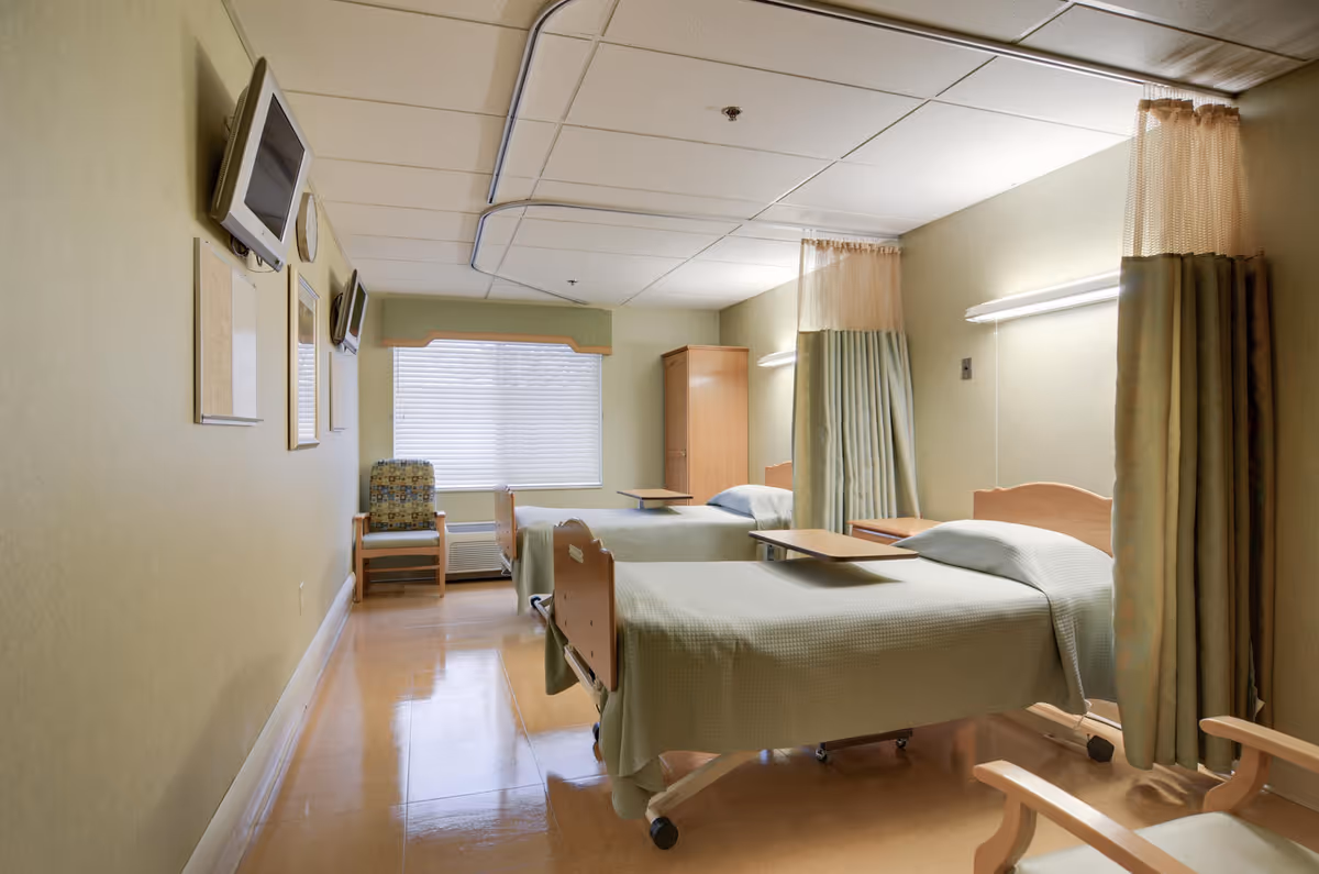 Two hospital beds with privacy curtains in a well-lit patient room.