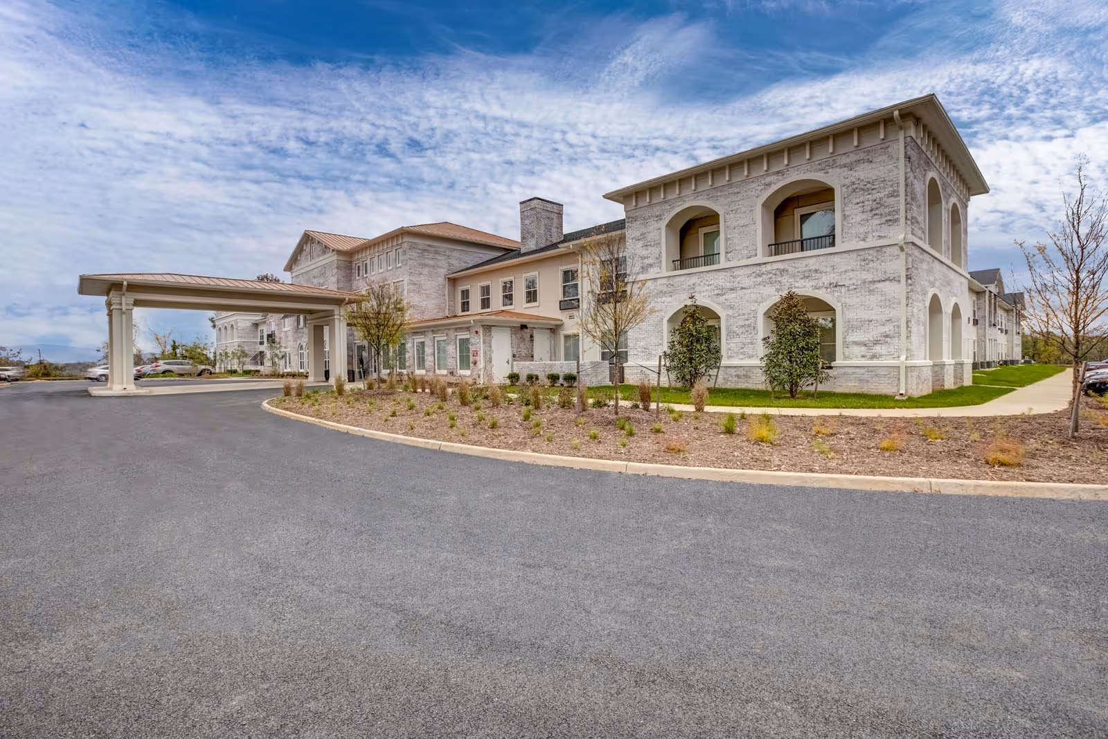 Exterior view of a modern senior living building with a curved driveway and landscaped entrance.