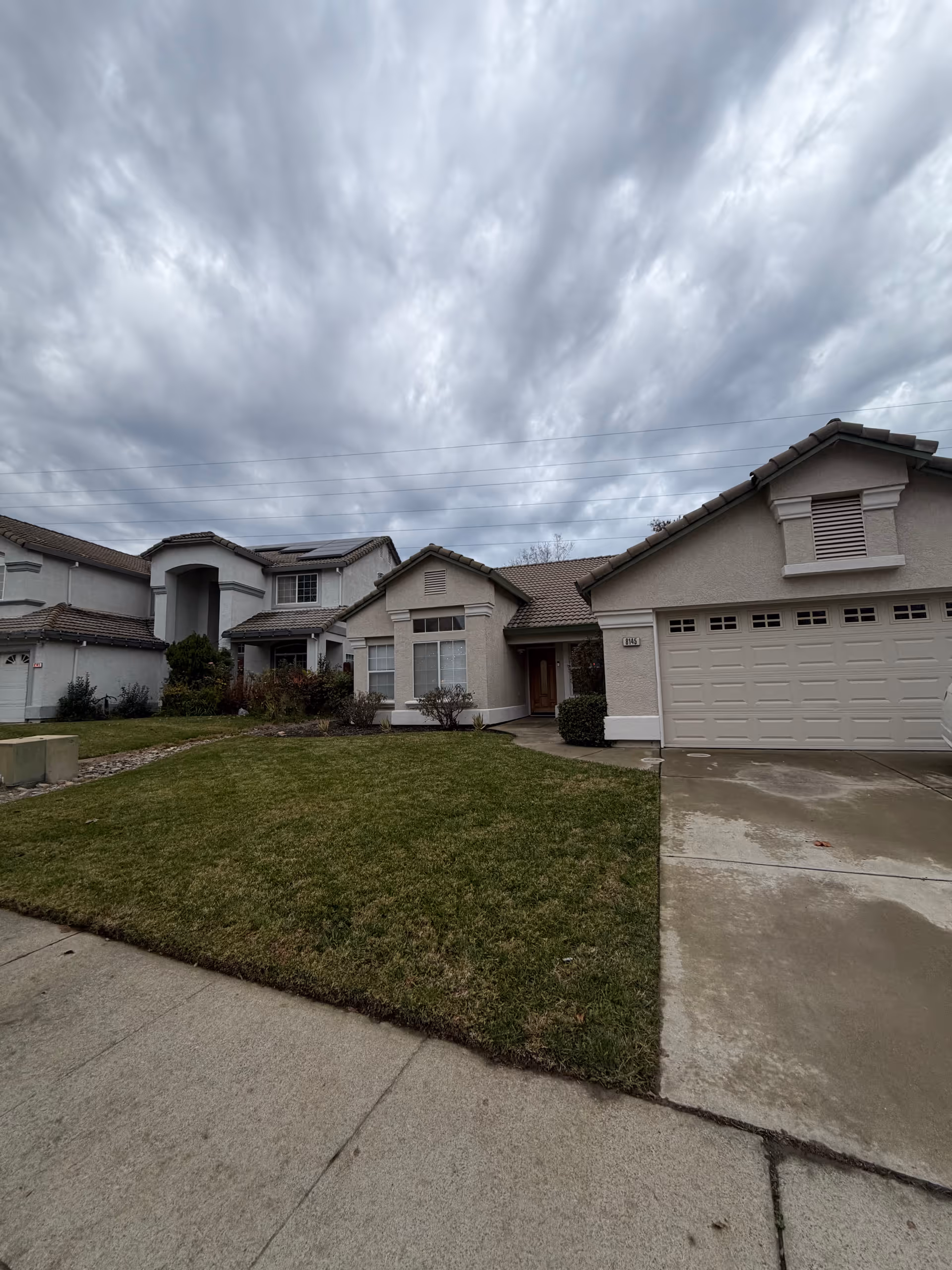 Residential-style senior care facility exterior with a lawn, driveway, and double garage.