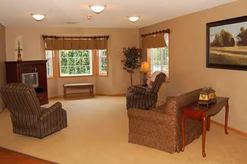 Cozy memory care living room with chairs, sofa, lamp, and large windows.