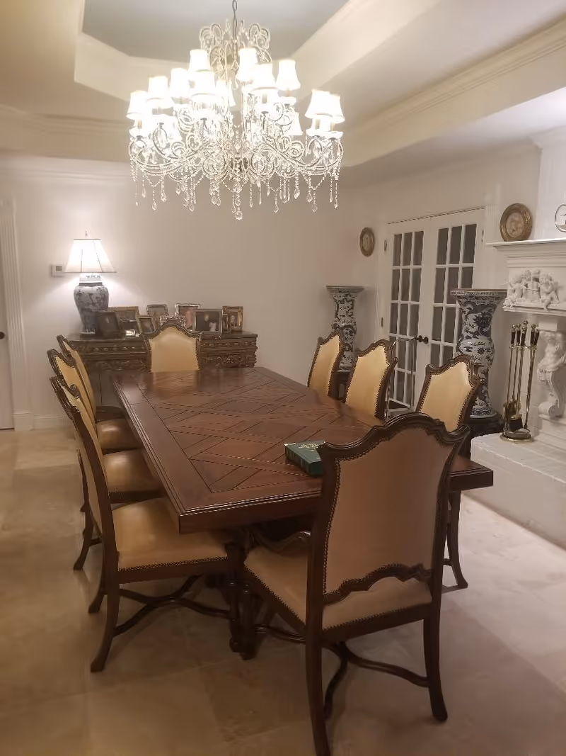 Elegant dining room with a large wooden table, beige chairs, and a crystal chandelier.