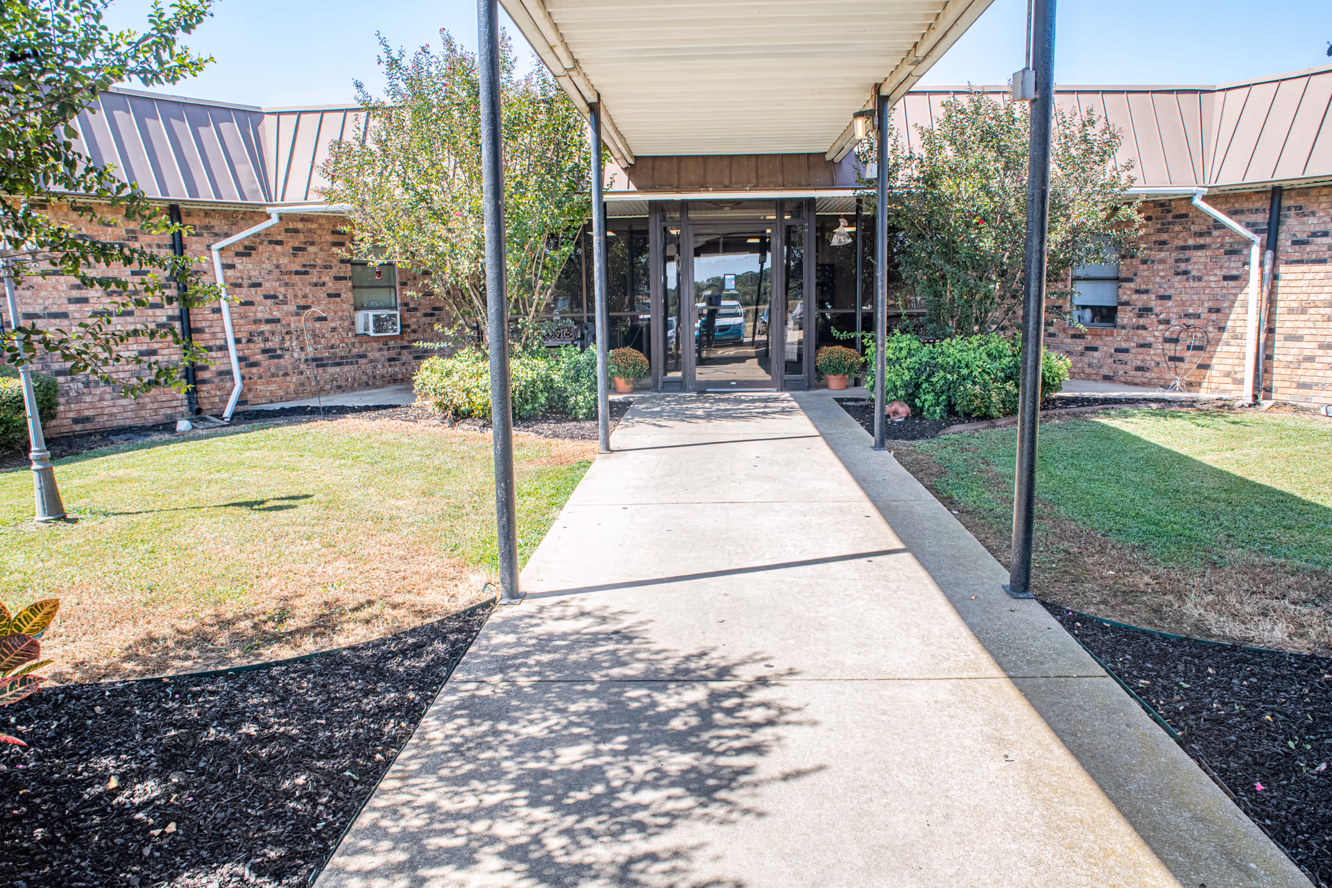 Brick senior living facility entrance with glass doors, covered walkway, and landscaped sides.