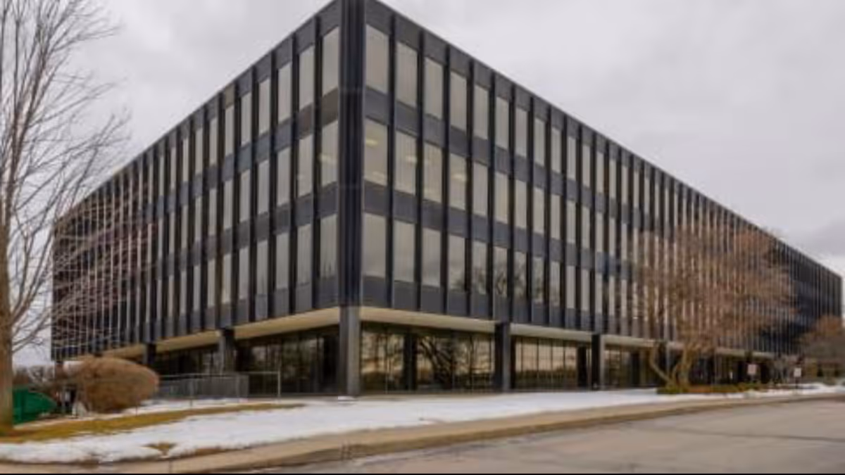 Modern multi-story glass-front building with dark frames, snow on ground, street in front.