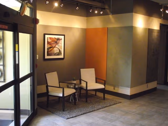 A modern lobby seating area with two chairs, a small table, and abstract art.